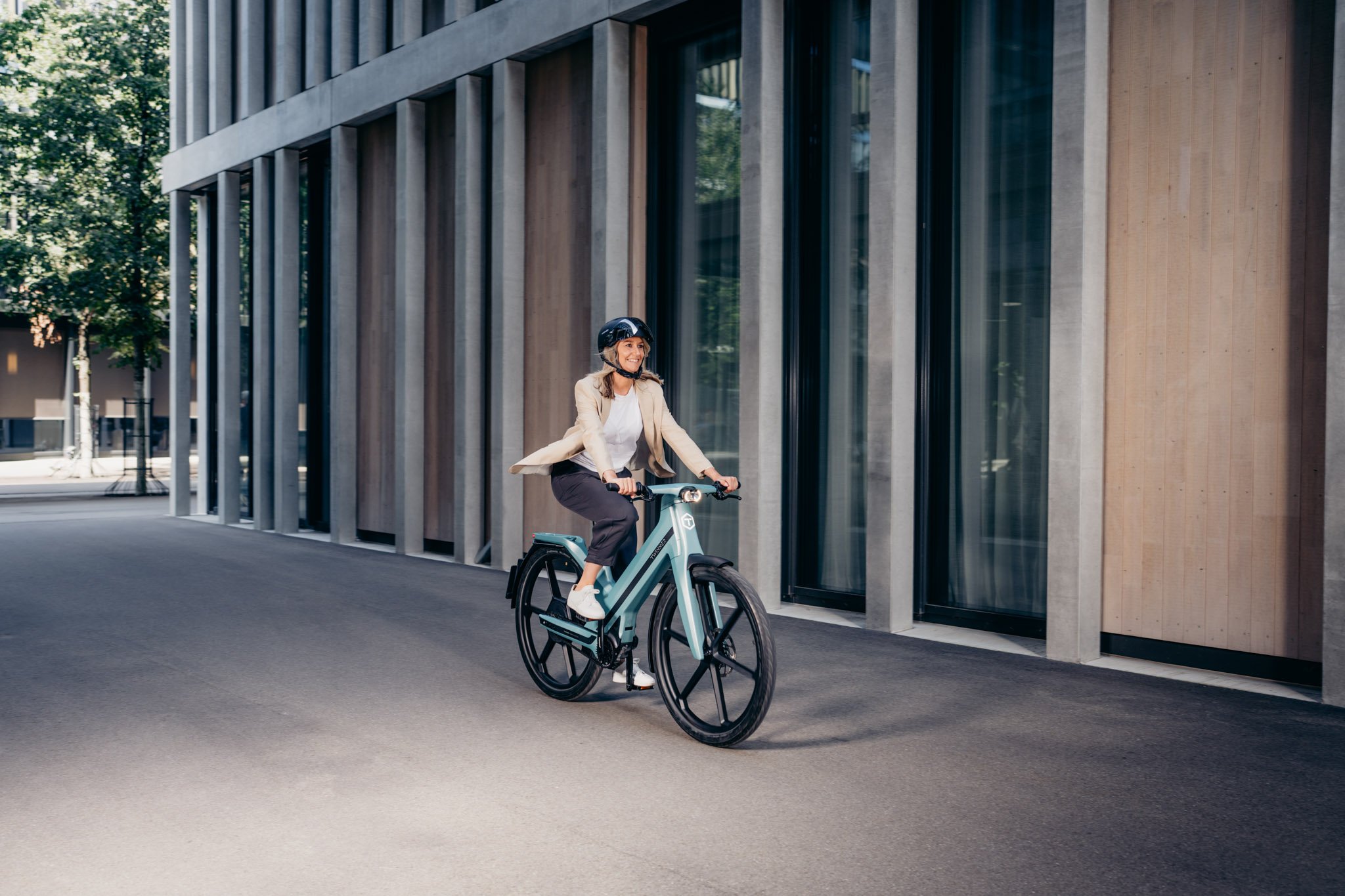 Frau in Business Outfit und Helm fährt auf Ice Blue Twinner E-Bike