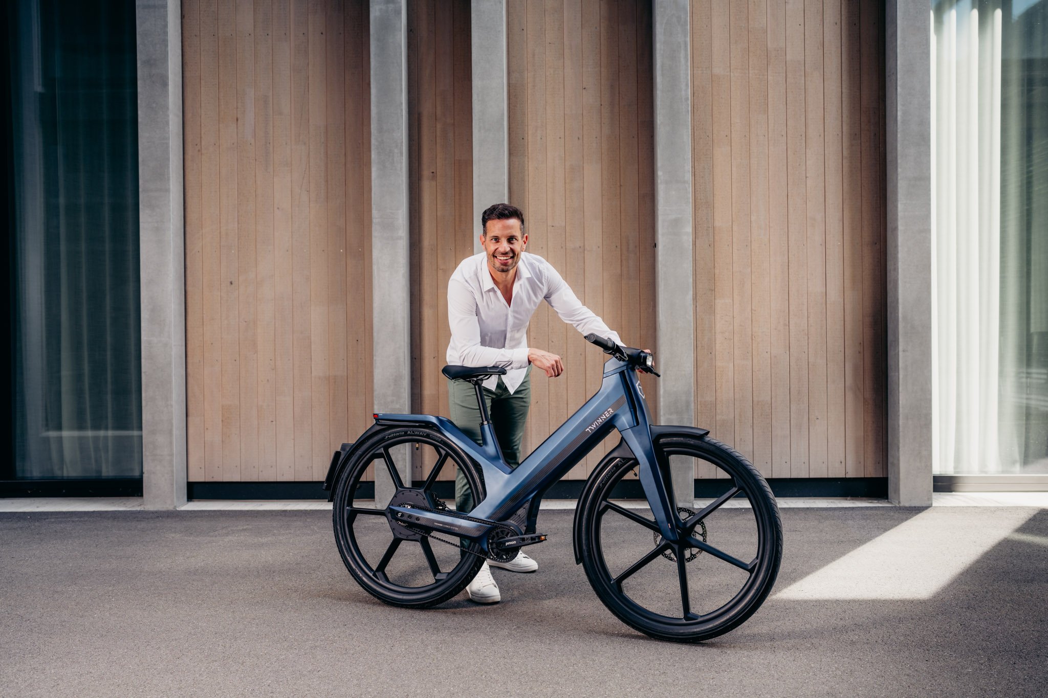 Mann in weissem Hemd stützt sich auf blauem Twinner E-Bike ab