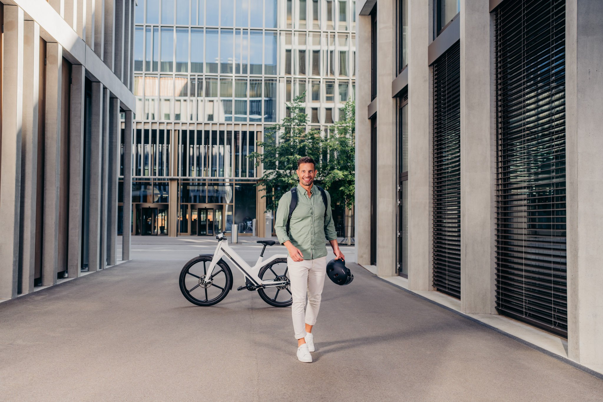 Mann in urbaner Gegend, Rucksack auf dem Rücken, Helm in der Hand, Twinner E-Bike im Hintergrund